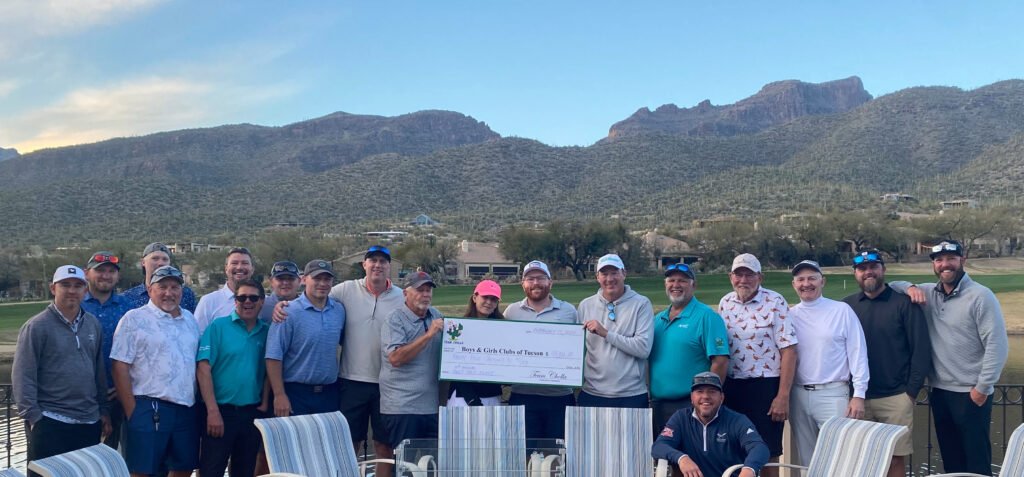 Team-Cholla-check-presentation-2024-cropped – Boys & Girls Clubs of the Gila Valley A large group of men and women are smiling for the camera and holding a large-format check. The golf course, mountains, and blue sky are in the background.